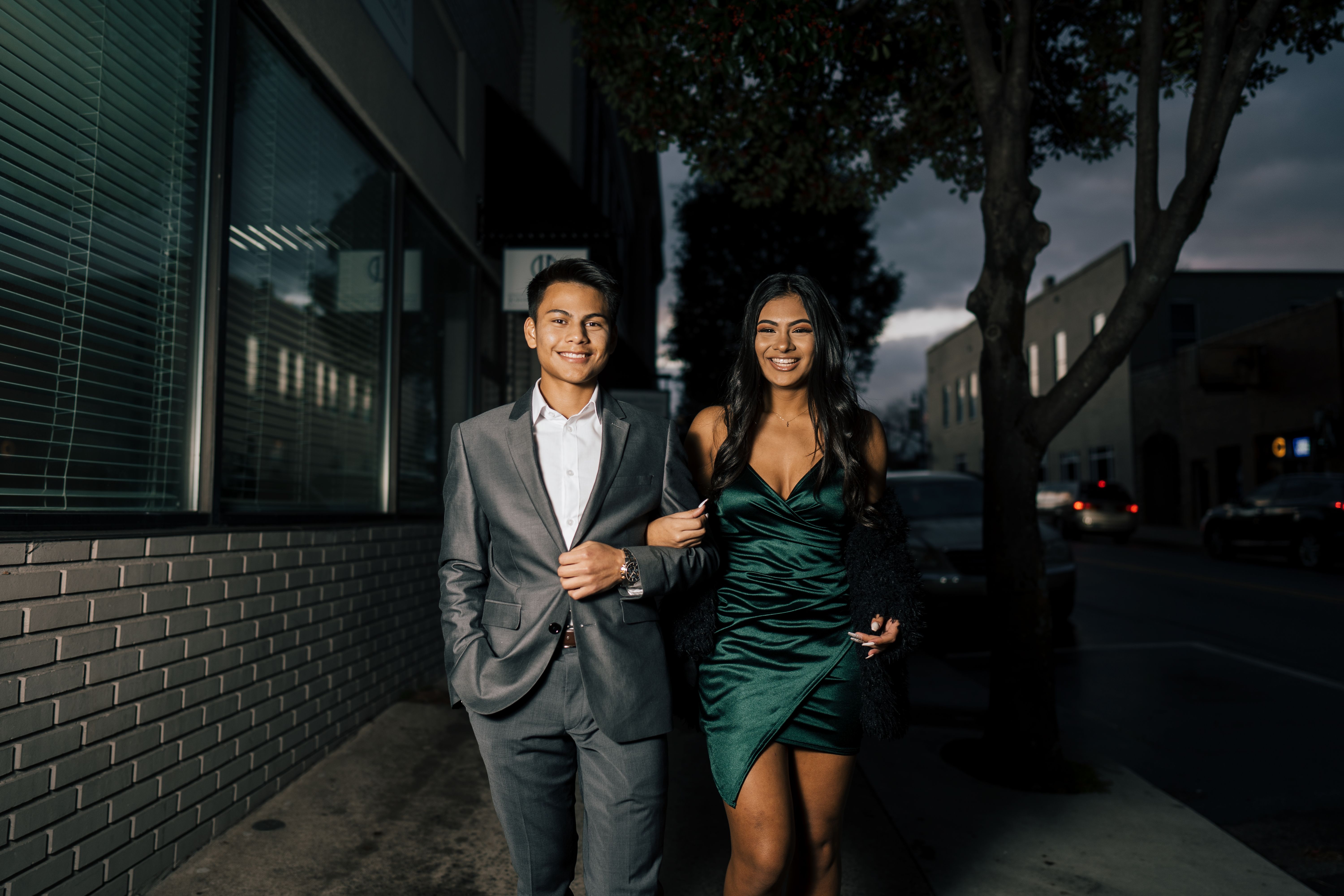 Stylish couple walking arm in arm on a city sidewalk at night in formal attire after a date