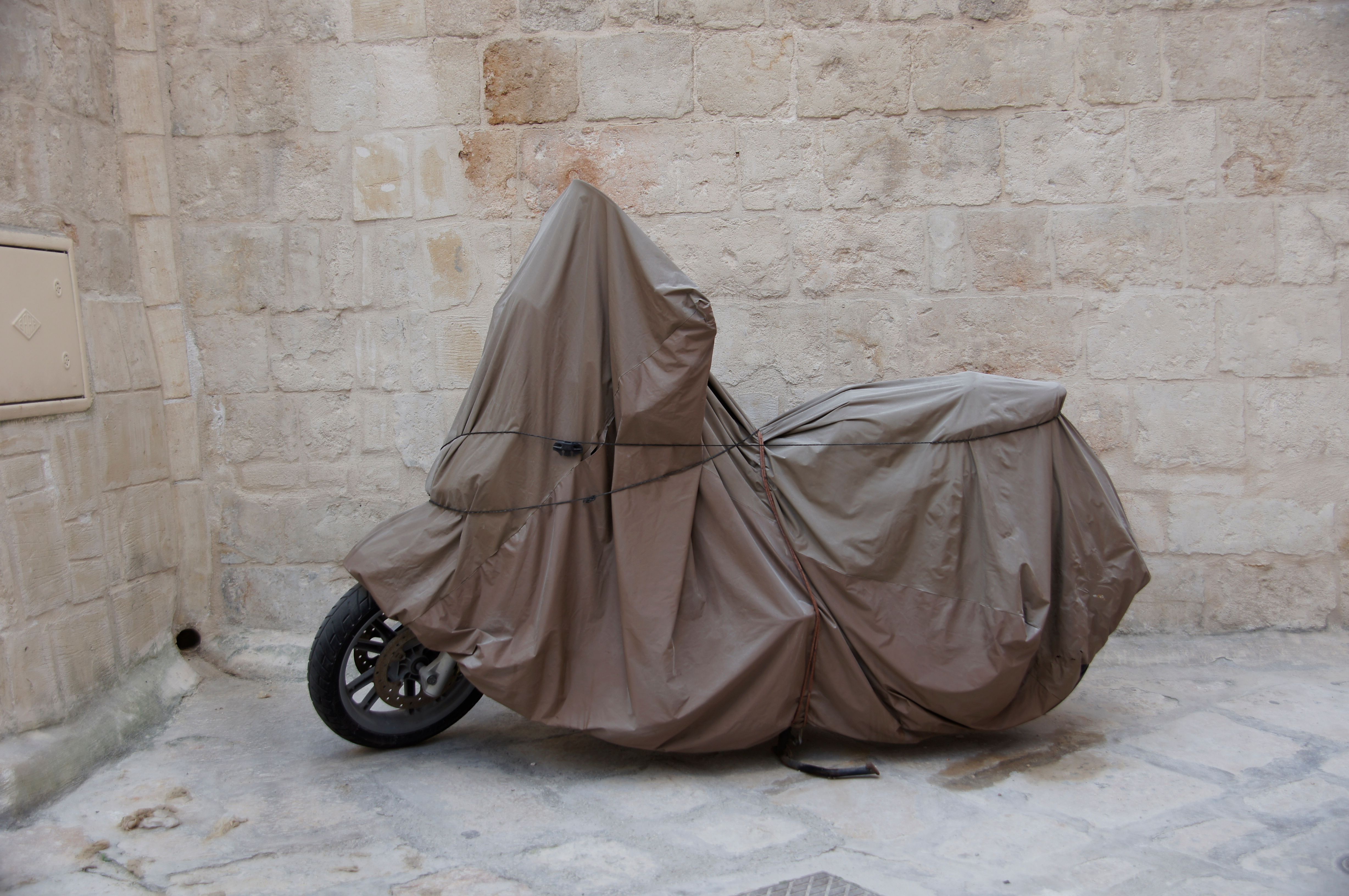Motorcycle parked under a protective tarp cover to shield it from sun and weather