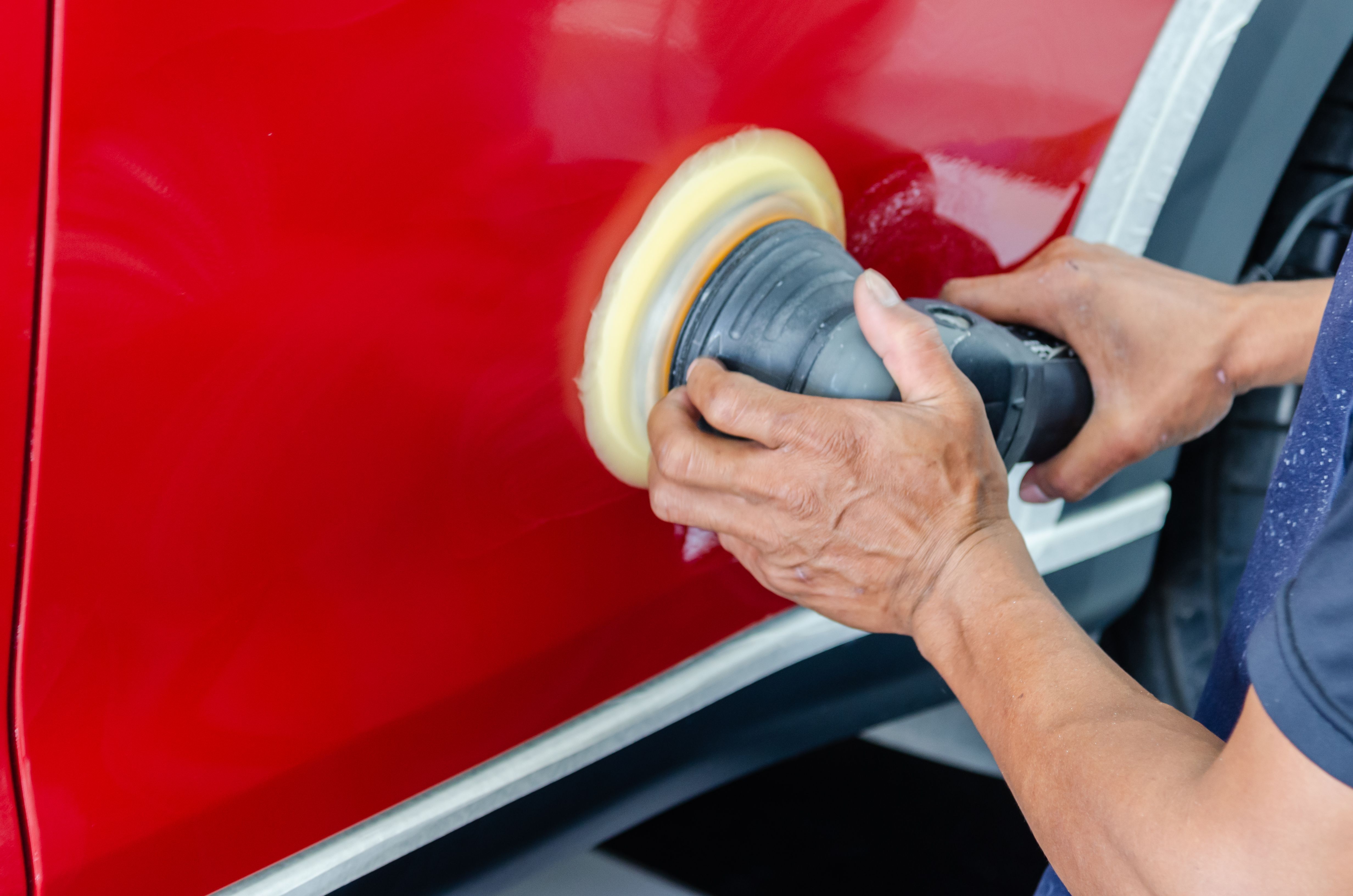 Worker buffing and polishing a red painted surface with a machine for paint protection and shine