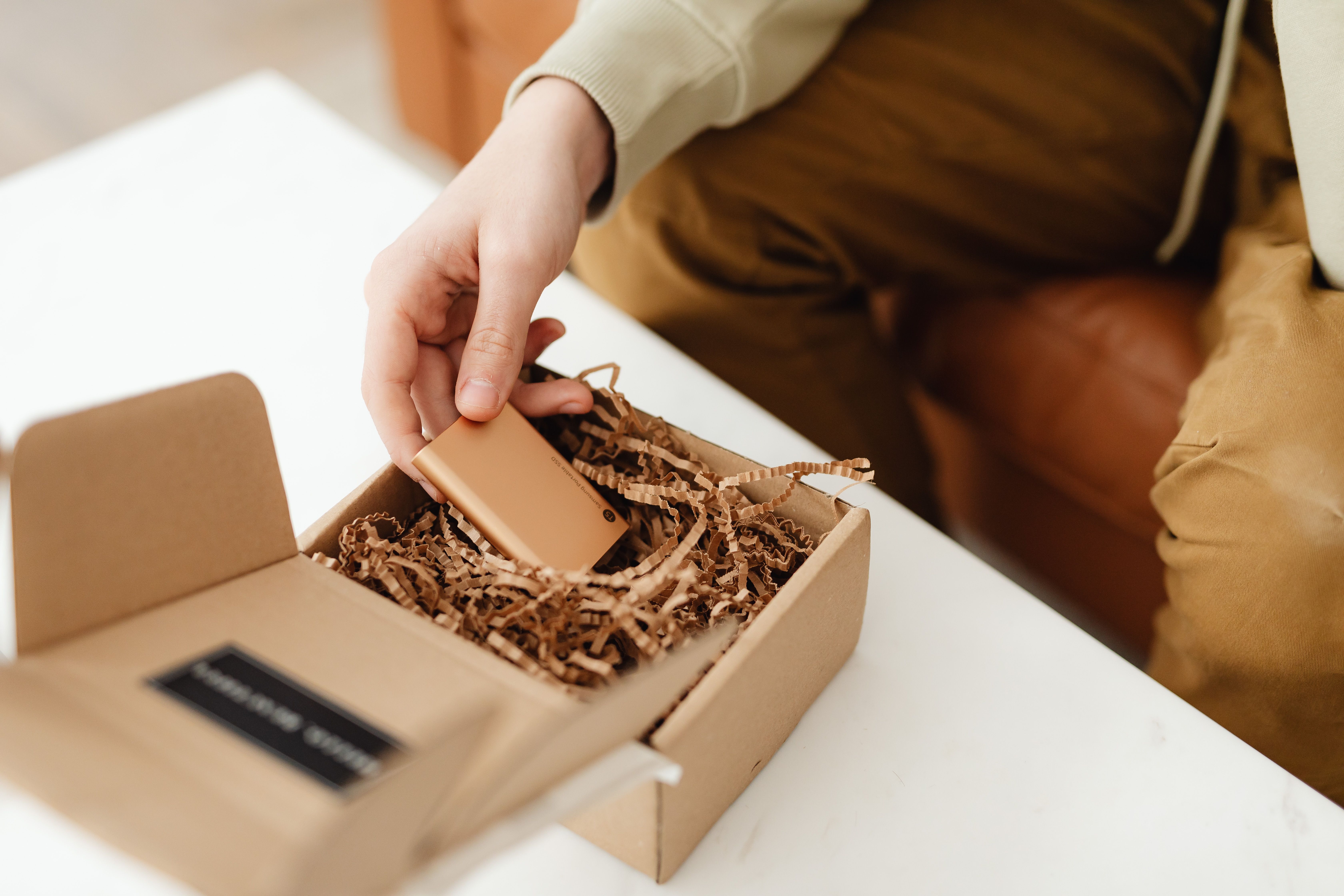 Hand unboxing a small item from a cardboard package filled with protective crinkle paper