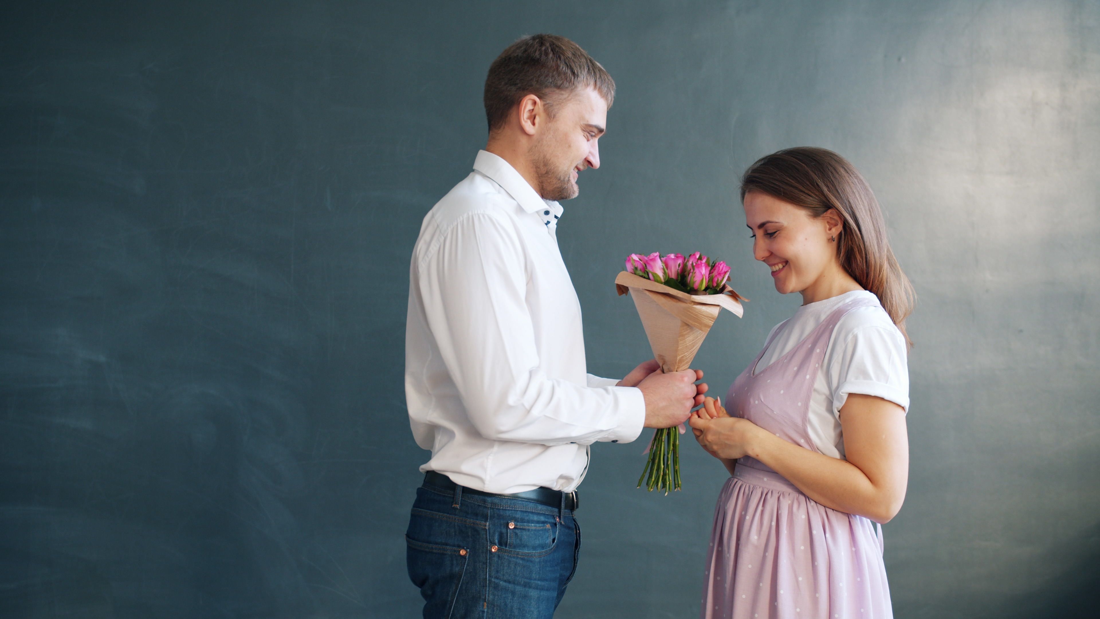 Man in white shirt presenting a bouquet of flowers to a smiling woman as a thoughtful romantic gesture